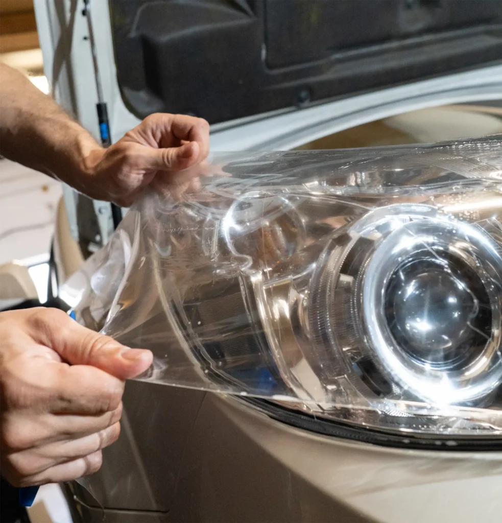 Ruce zaměstnance Miracle Garage Tábor, natahující čirou PPF folii na světlomety auta při detailingové renovaci světel.